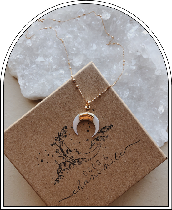 crescent moon necklace with gold chain sitting on top of brown kraft gift box